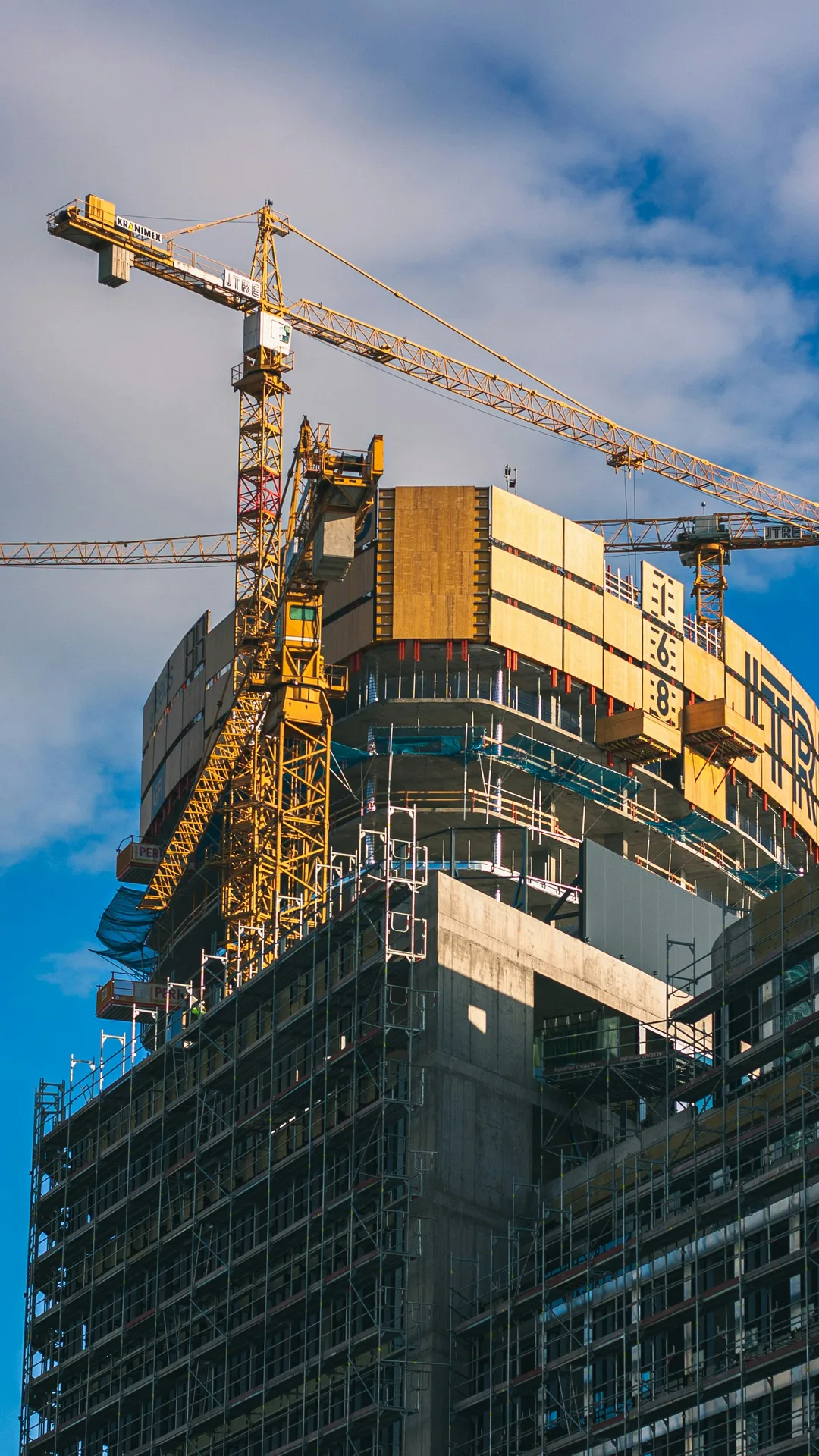 Unusually shaped (squares and ovals) building under construction with scaffolding and tower cranes as it approaches topping out