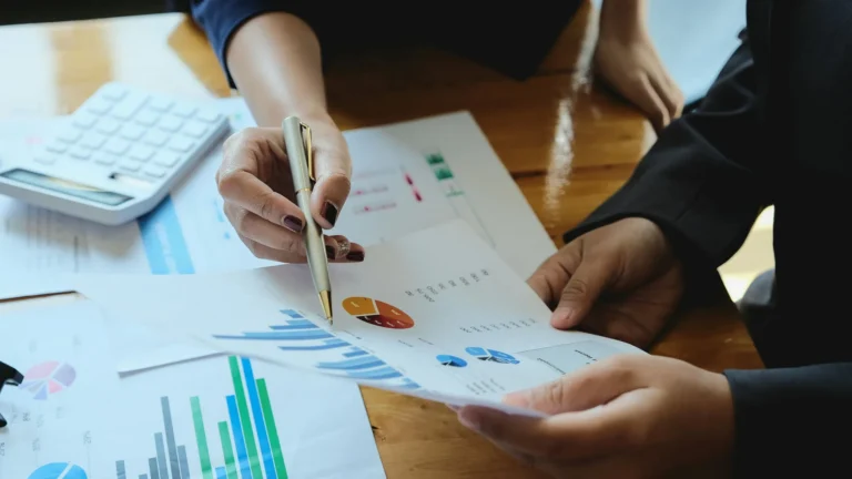 Two people discussing bar and pie charts on a printout and indicating at one data point