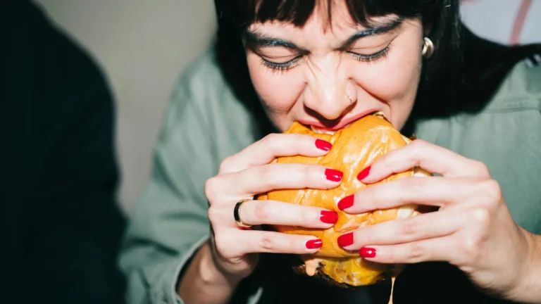 Woman taking a big bite out of a large cheeseburger